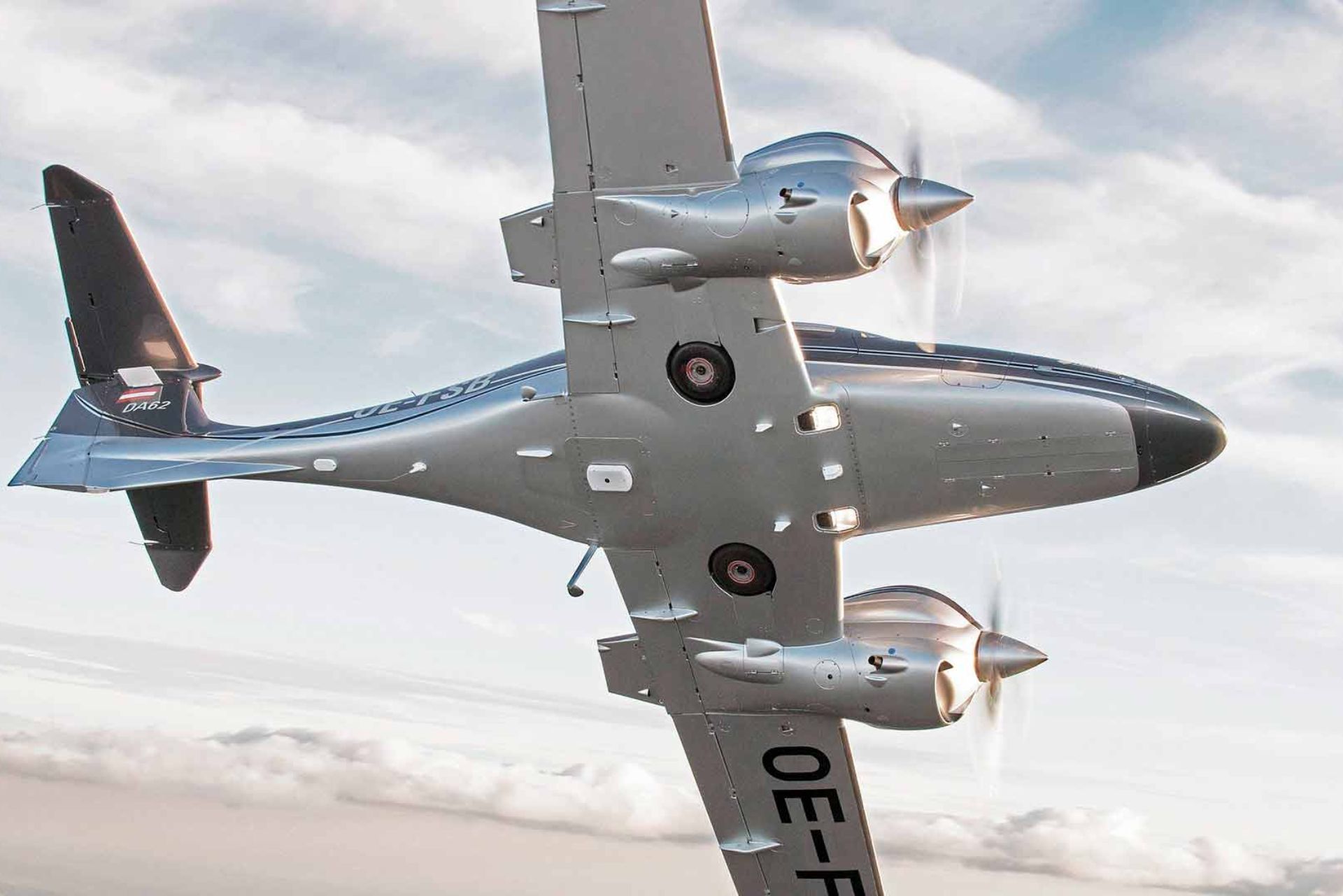 Diamond DA62 twin-engine aircraft bottom view with spinning propellers in flight.