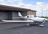 A white and grey single-engine propeller plane, registration number N603DG, parked on an asphalt tarmac in front of an open hangar, under a partly cloudy sky.