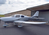A white and grey single-engine propeller plane, registration number N603DG, parked on an asphalt tarmac in front of an open hangar, under a partly cloudy sky.