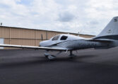 A white and grey single-engine propeller plane, registration number N603DG, parked on an asphalt tarmac in front of an open hangar, under a partly cloudy sky.