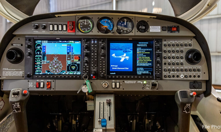 A straight-on view of an aircraft cockpit, registration NB33DB, featuring dual control sticks and a hybrid instrument panel with digital displays and analog gauges.