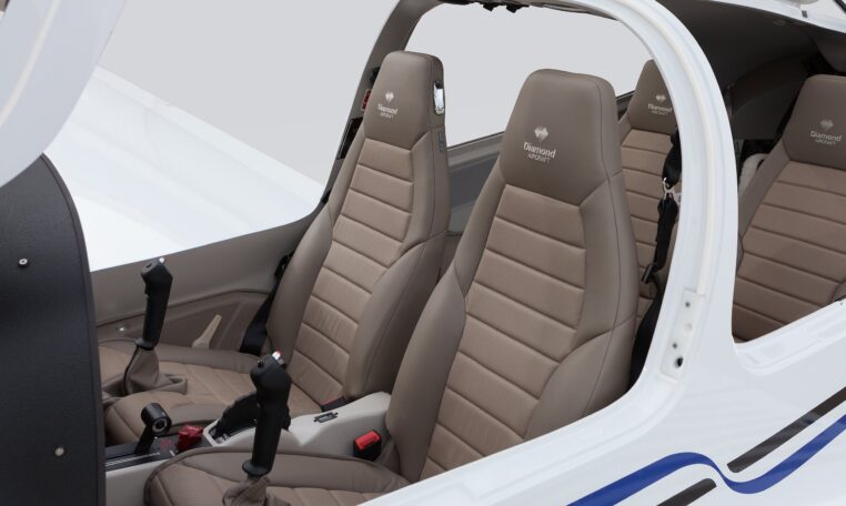 The interior cabin of a modern aircraft, showing four taupe leather seats embroidered with "Diamond Aircraft" and two control sticks.