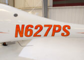 Close-up of white aircraft with orange tail number N627PS in a hangar, showing fuselage registration markings.