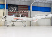 White light aircraft in hangar, side view of single-engine prop plane with orange accents under Premier sign.