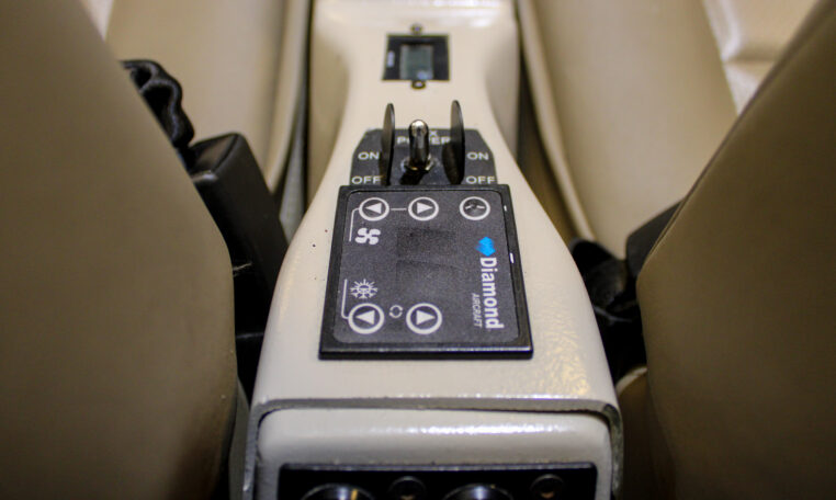 Diamond Aircraft cockpit center console with climate control panel, power switches, and beige leather seats.