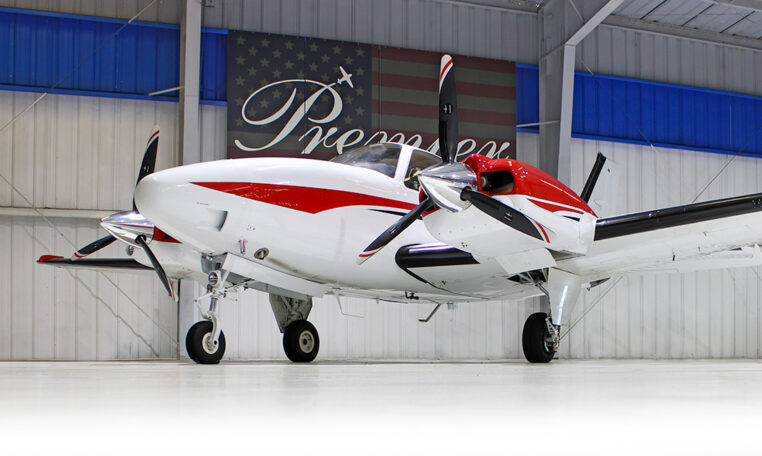 Red and white twin-engine propeller airplane in hangar at Premier, private aircraft for sale
