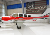 Red and white twin-engine propeller aircraft in Premier Aircraft hangar, side view on glossy white floor.