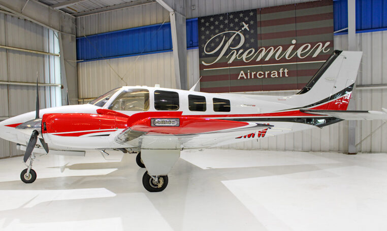 Red and white twin-engine propeller aircraft in Premier Aircraft hangar, side view on glossy white floor.