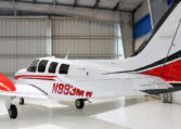 Beechcraft Bonanza single-engine airplane in a hangar, white with red accents, private aircraft side view.