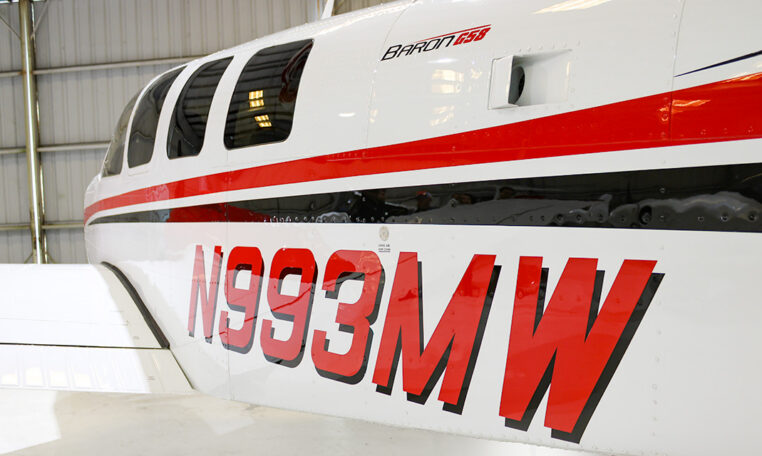 Beechcraft Baron G58 aircraft close-up showing red stripe and registration N993MW inside hangar.