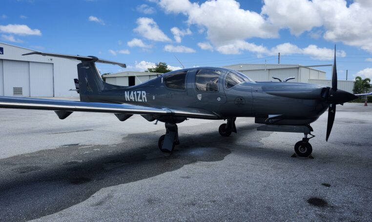 Dark gray single-engine propeller aircraft on airport tarmac near hangars, sleek T-tail design, tail number N41ZR.