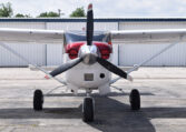 Front view of light single-engine high-wing propeller plane parked on airport tarmac in front of a hangar
