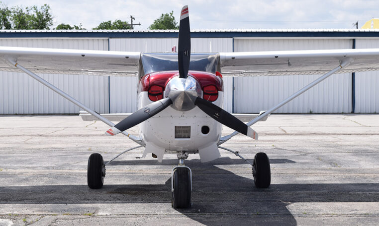 Front view of light single-engine high-wing propeller plane parked on airport tarmac in front of a hangar