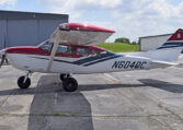Red and white Cessna single-engine high-wing airplane N604DC parked on airport tarmac by hangars.