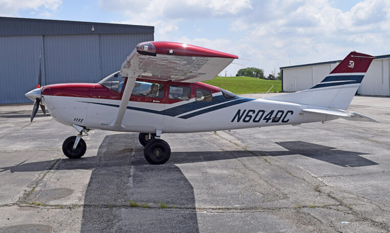 Red and white Cessna single-engine high-wing airplane N604DC parked on airport tarmac by hangars.