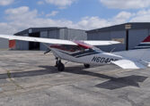 High-wing single-engine taildragger general aviation airplane parked by hangars on tarmac under blue sky