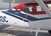 Close-up of red, white and blue Cessna single-engine airplane fuselage and windows parked on airport tarmac.