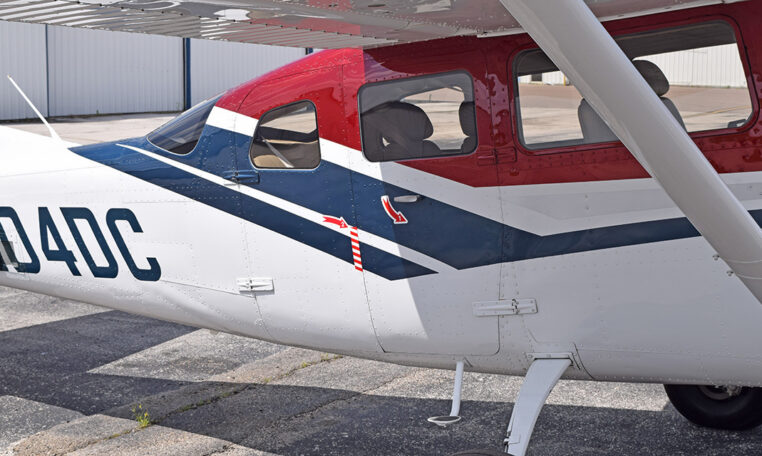 Close-up of red, white and blue Cessna single-engine airplane fuselage and windows parked on airport tarmac.