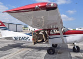 Red and white Cessna high-wing single-engine airplane on airport ramp, cabin door open for boarding.