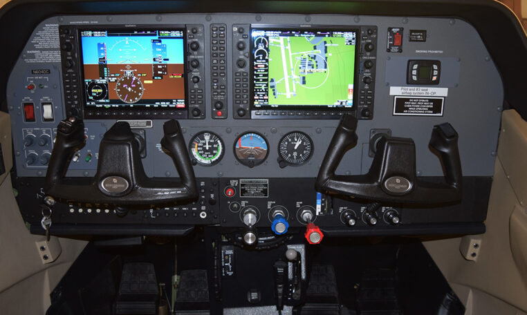 Light aircraft cockpit with dual Garmin G1000 displays, yokes and flight instruments on instrument panel.