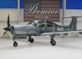 Sleek gray single-engine propeller plane in hangar at Premier Aircraft with American flag backdrop