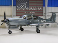 Sleek gray single-engine propeller plane in hangar at Premier Aircraft with American flag backdrop