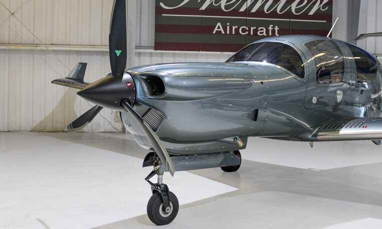 Modern metallic gray single-engine propeller aircraft in Premier Aircraft hangar, nose and landing gear close-up