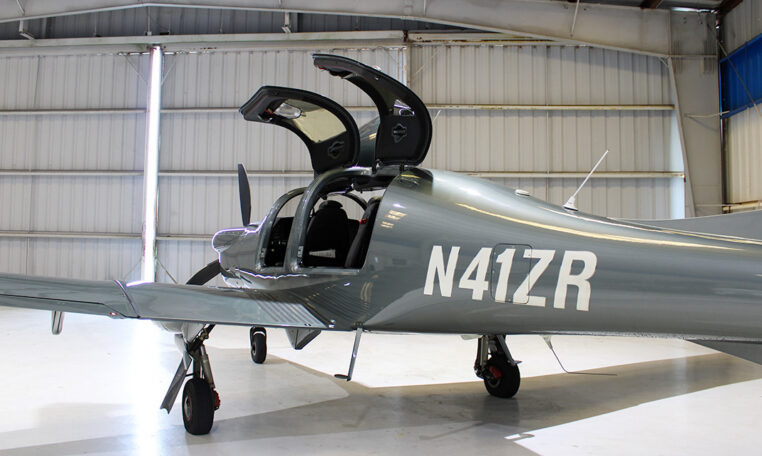 Gray Cirrus SR22 single-engine plane in hangar with gullwing doors open, N41ZR visible, modern private aircraft interior.
