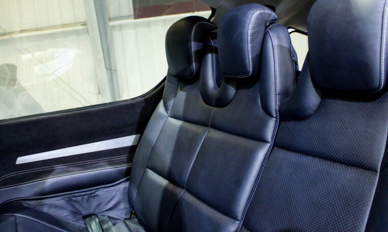 Luxury car rear seats in black perforated leather with adjustable headrests and contrast stitching, premium interior.