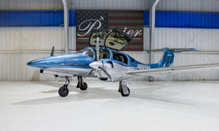 Blue and silver twin-engine propeller airplane in a hangar with gullwing doors open, private aircraft N895PA