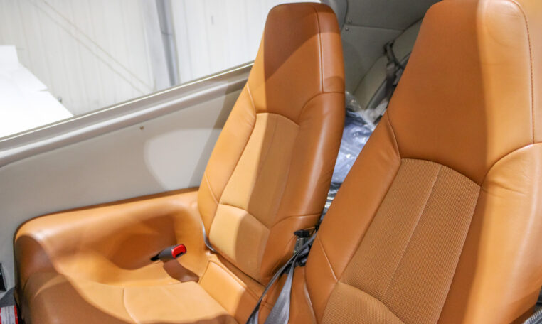 Private airplane interior with two tan leather seats and seat belts in a light aircraft cabin.