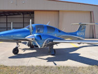 Blue twin-engine propeller aircraft parked outside an airport hangar, private plane ready for flight training or travel.