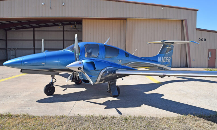 Blue twin-engine propeller aircraft parked outside an airport hangar, private plane ready for flight training or travel.