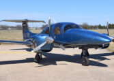 Blue twin-engine propeller aircraft parked on airport tarmac under clear sky, private plane exterior front view.