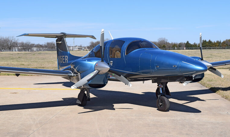 Blue twin-engine propeller aircraft parked on airport tarmac under clear sky, private plane exterior front view.