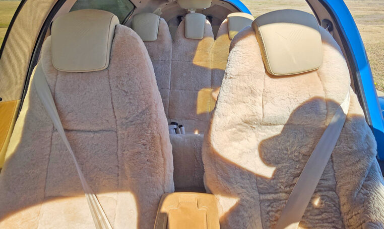 Light airplane interior with plush sheepskin seat covers; four-seat cabin, seatbelts and headrests in sunlight.