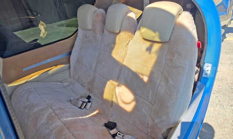 Small airplane rear bench with tan sheepskin seat covers, three headrests and seatbelts in sunlit cabin