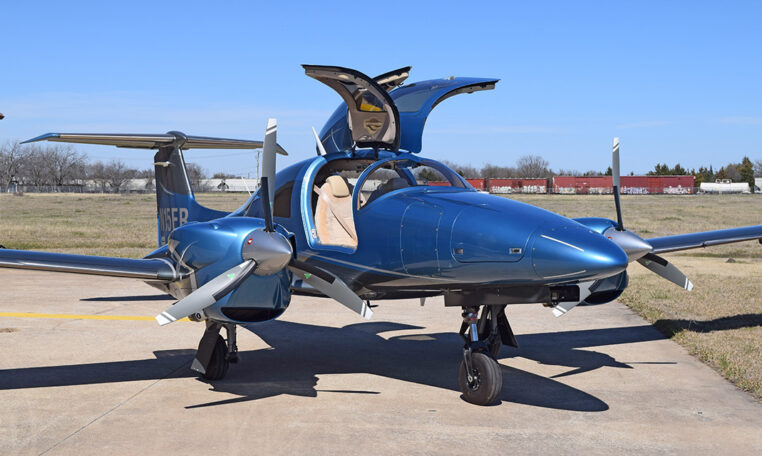 Sleek blue twin-engine propeller private plane with gullwing doors open on airport tarmac.
