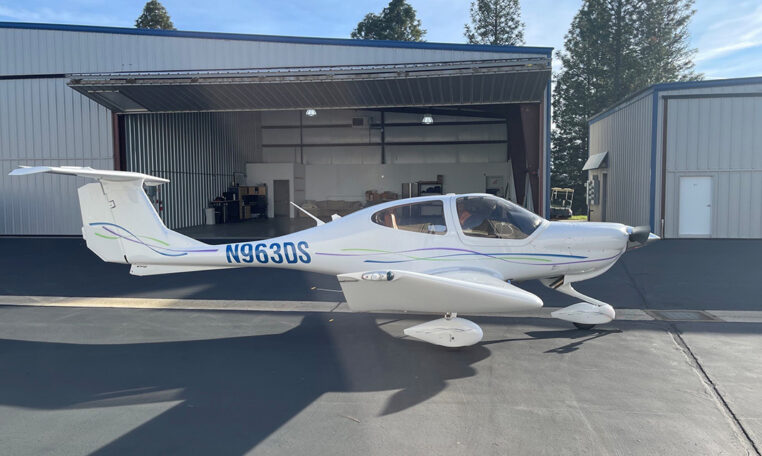 White single-engine propeller plane N963DS outside an open hangar at a small airport on a sunny day.