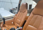Airplane cockpit interior with two tan leather seats and joystick controls inside a hangar