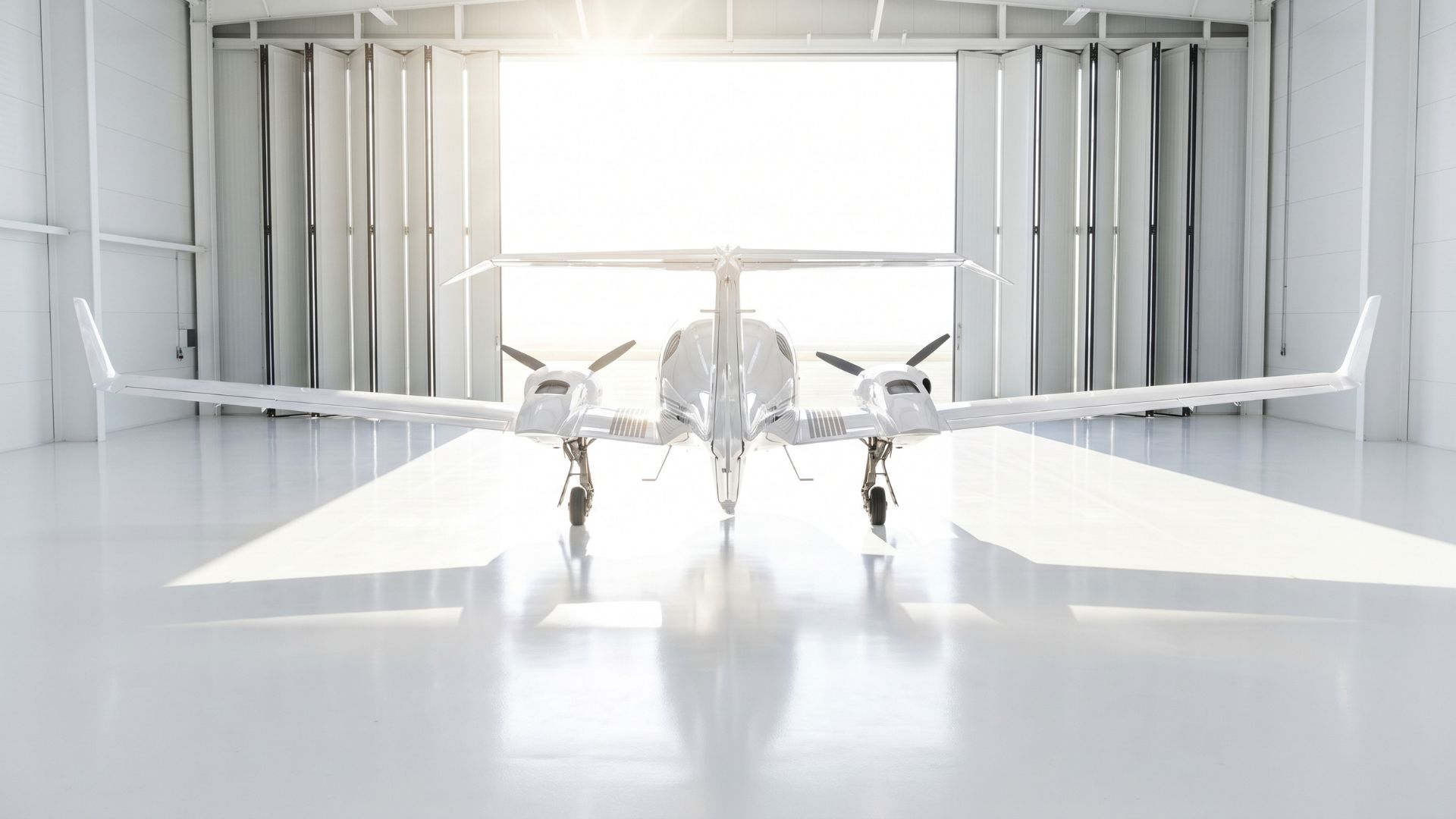 Sleek twin-engine propeller aircraft in bright hangar, front view with sunlit doorway, private plane ready for flight.