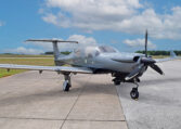 Modern light single-engine propeller aircraft parked on airport tarmac, ready for takeoff under blue skies.