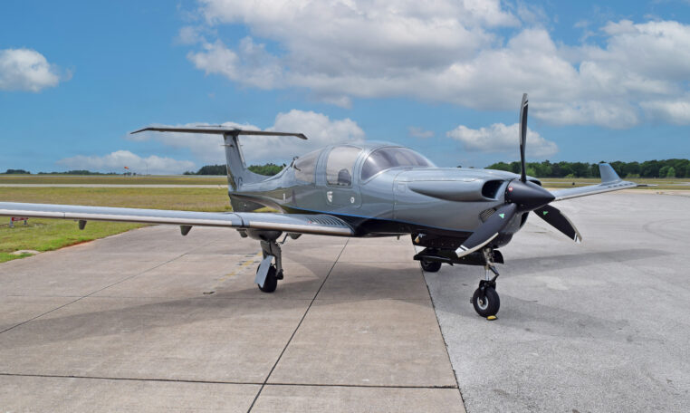 Modern light single-engine propeller aircraft parked on airport tarmac, ready for takeoff under blue skies.