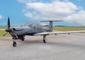 Modern single-engine propeller airplane on airport tarmac, sleek gray private plane under blue sky with clouds