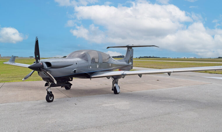 Modern single-engine propeller airplane on airport tarmac, sleek gray private plane under blue sky with clouds
