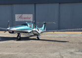 Teal and silver twin-engine private propeller airplane on tarmac at Premier Aircraft Sales hangar, front view