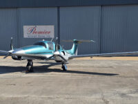 Teal and silver twin-engine private propeller airplane on tarmac at Premier Aircraft Sales hangar, front view