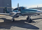 Teal twin-engine propeller aircraft parked on airport ramp near hangar under blue sky