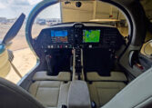 Modern light aircraft cockpit with glass cockpit avionics, dual displays and center console, parked in hangar.