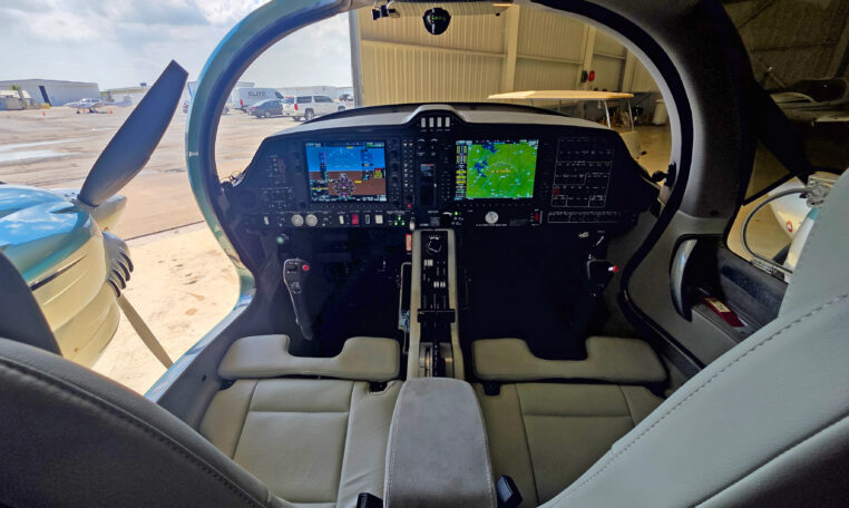 Modern light aircraft cockpit with glass cockpit avionics, dual displays and center console, parked in hangar.